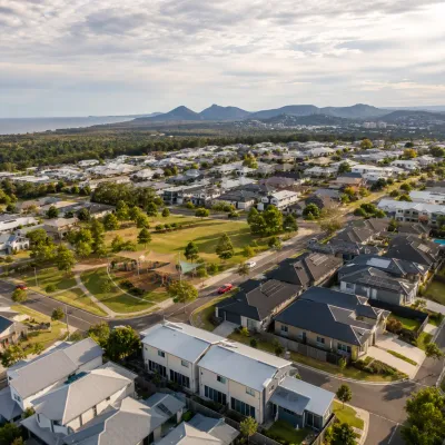 Drone view of a Sunshine Coast residential neighbourhood with modern homes, green parkland, mountain ranges and the coast in the distance, representing attractive suburbs for first home buyers.