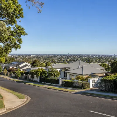 Real residential streetscape in Indooroopilly showing hillside homes, leafy surroundings, and suburban property views.