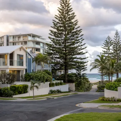 Palm Beach coastal homes and apartments beside a beach access street under natural cloudy skies, representing the suburb’s lifestyle appeal and property investment opportunities.