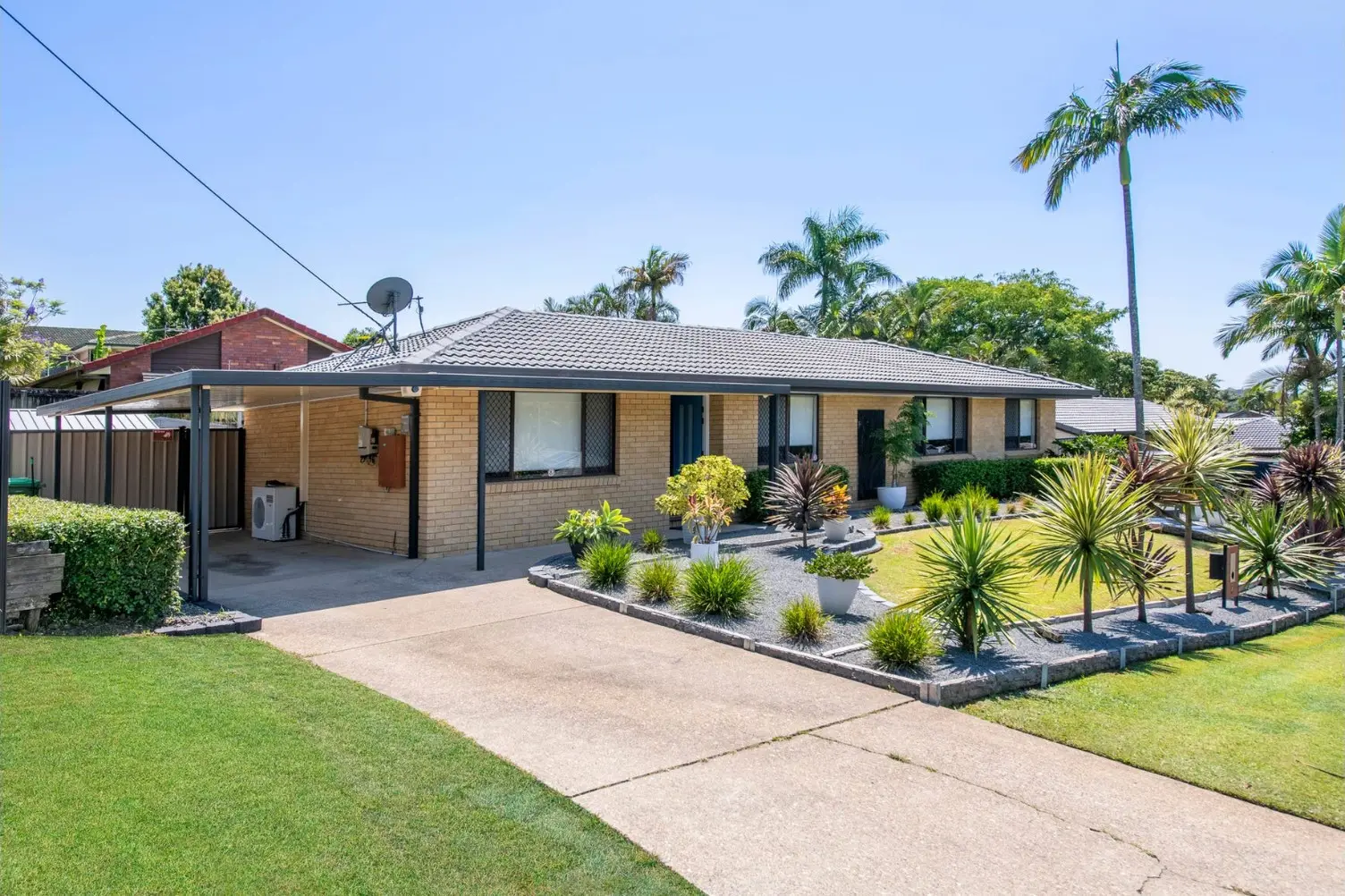 Brick home with a double carport, palm trees and a paved driveway at 2 Bushtree Court, Burleigh Waters