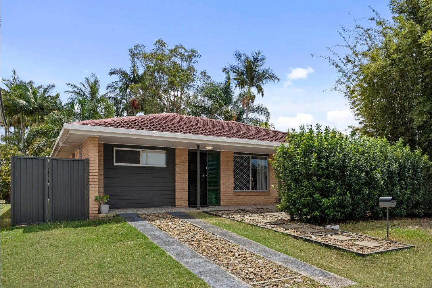 Low-set brick home with a paved path, hedges and palms at 61 Palm Beach Avenue, Palm Beach
