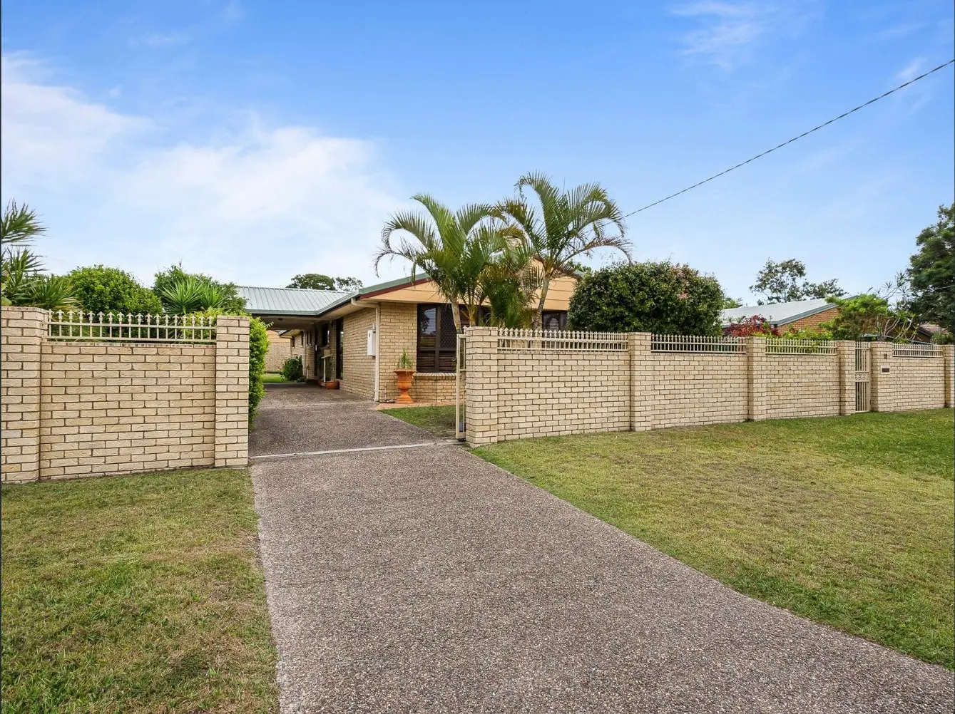 Blond-brick home behind a matching brick fence and a long driveway at 18 Tripcony Street, Bellara