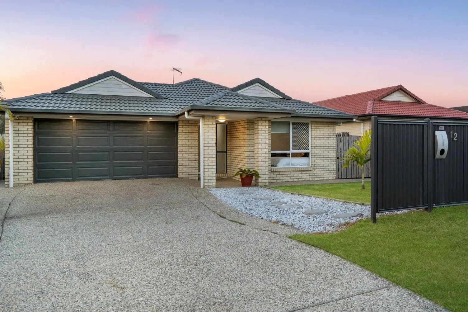 Brick single-storey home with a double garage and exposed-aggregate driveway at dusk, 12 Raleigh Place, Redbank Plains