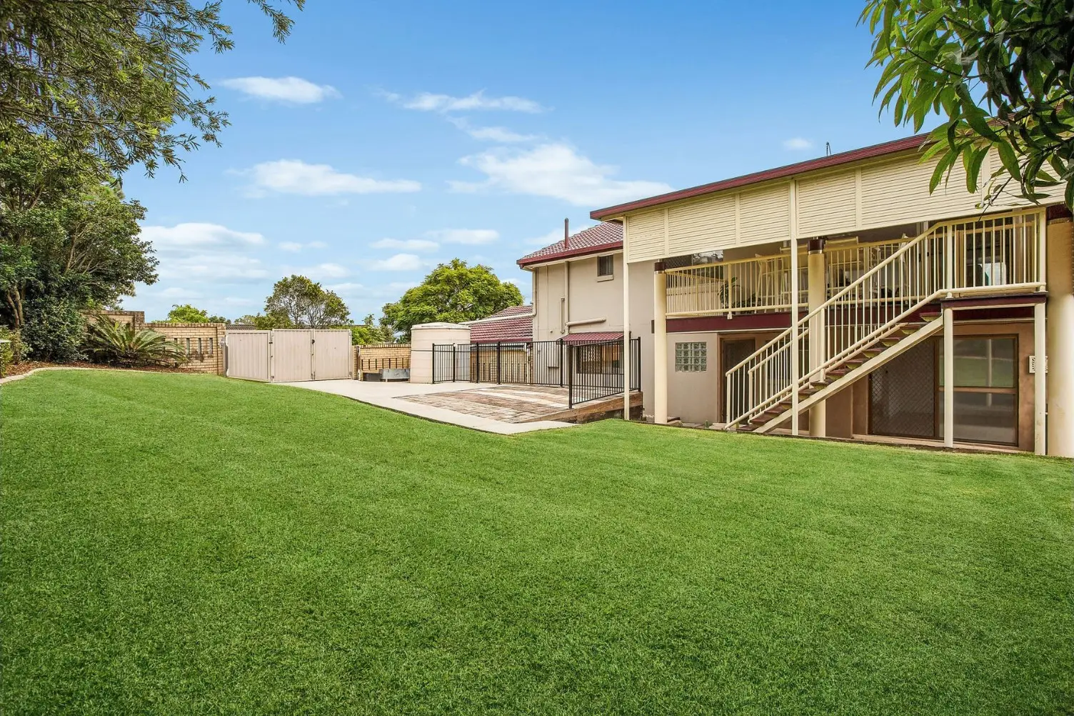 Two-storey home with an external staircase and a wide back lawn at 38 Ironbark Street, Elanora
