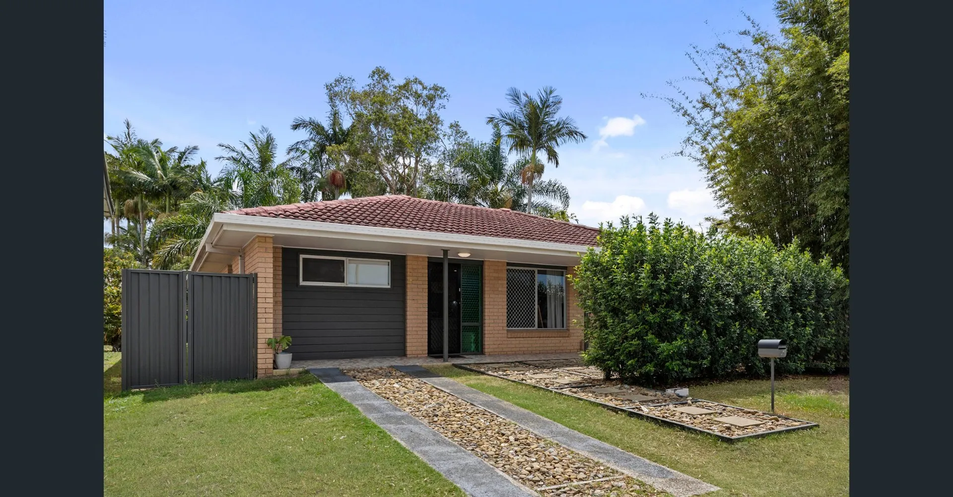 Low-set brick home with a paved path, hedges and palms at 61 Palm Beach Avenue, Palm Beach